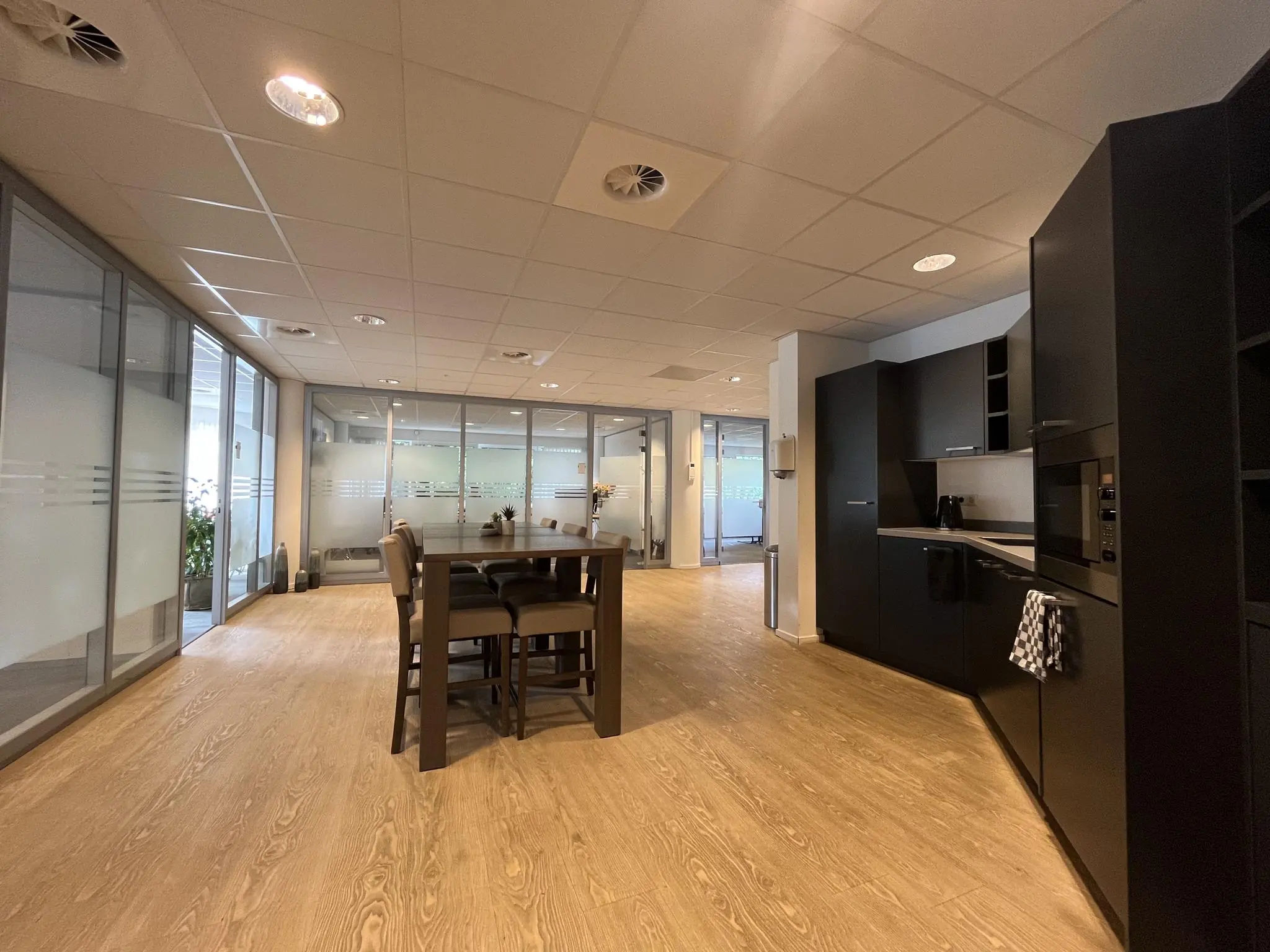 Moderne kantoorruimte aan de 1e Hogeweg met glazen wanden, een zwarte keuken en een hoge eettafel met stoelen.